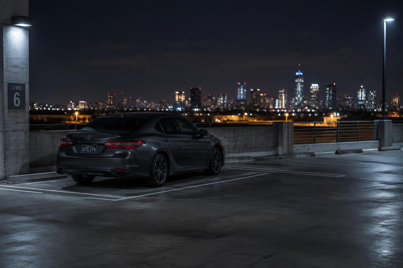 A dark sedan parked on the upper deck of a concrete parking garage at night